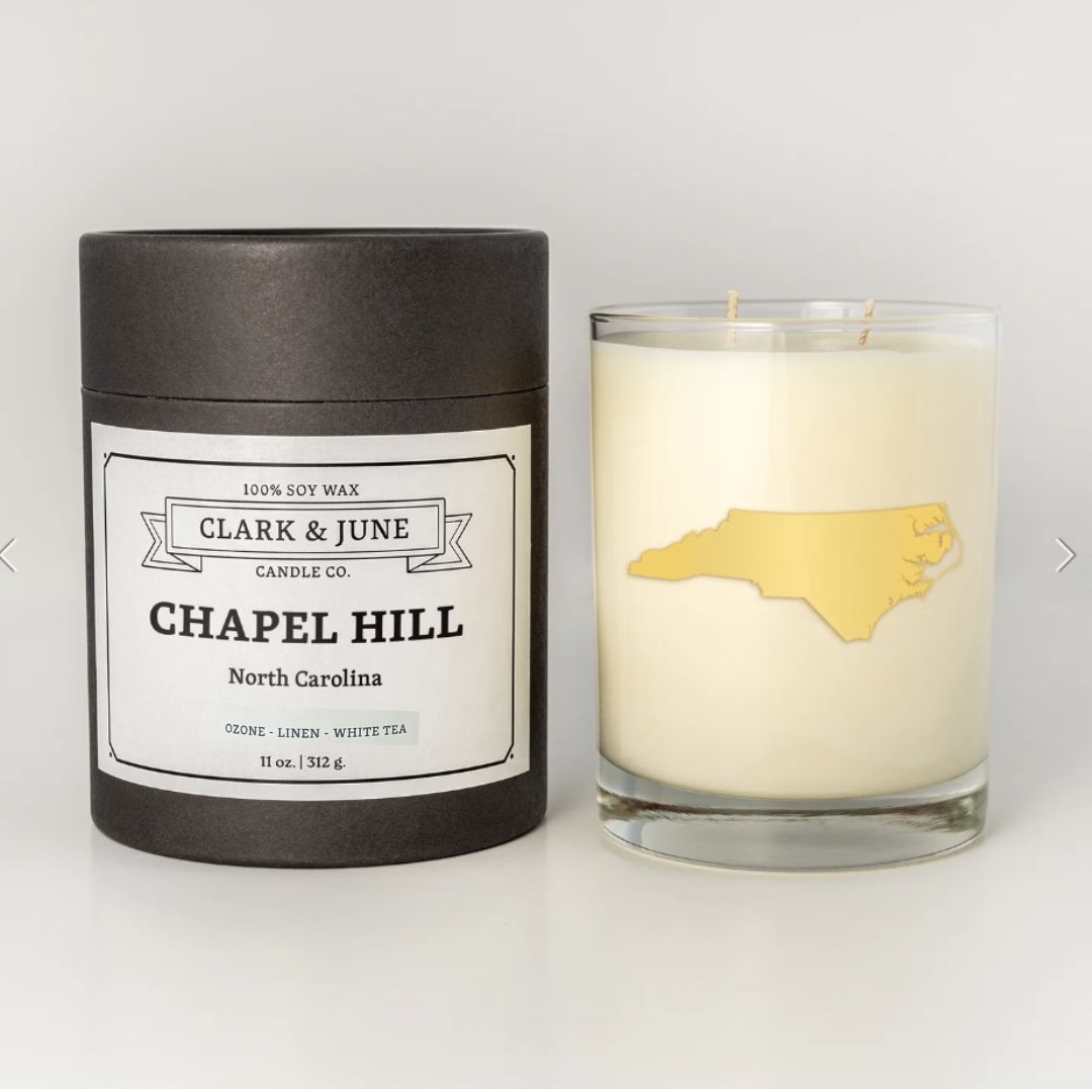Chapel Hill candle with a 22k gold foil silhouette of North Carolina, sitting next to its elegant black tube packaging labeled 'Chapel Hill'.