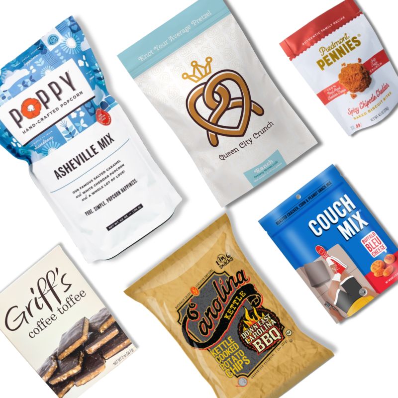 Flat lay of the Carolina Snack Box contents including NC-made popcorn, chips, granola, cookies, toffee, and snack mix, arranged neatly on a white background