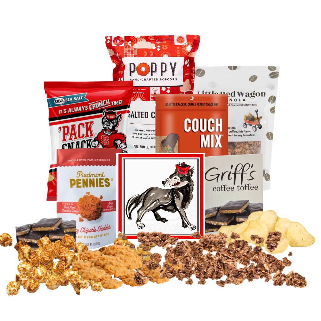 NC State-themed gift basket contents arranged on a countertop with small piles of each snack in front, showcasing red-packaged North Carolina-made gourmet treats