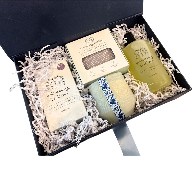Open navy luxury gift box displaying lavender self-care items including a soy candle, linen spray, body wash, and eye pillow—perfect for relaxation and gifting