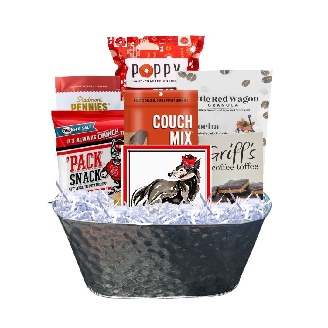 Assembled NC State-themed gourmet gift basket in a hammered tin planter, featuring red-packaged North Carolina-made snacks and watercolor wolf beverage napkins