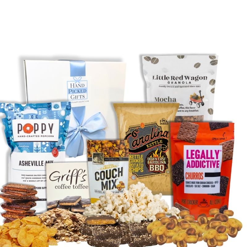 Carolina Snack Box with the white gift box displayed behind an arrangement of North Carolina-made gourmet snacks including popcorn, chips, cookies, granola, and toffee