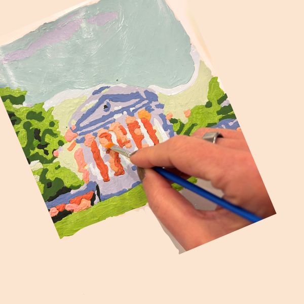 Hand painting a colorful scene of UVA's rotunda on a small canvas with a blue brush.