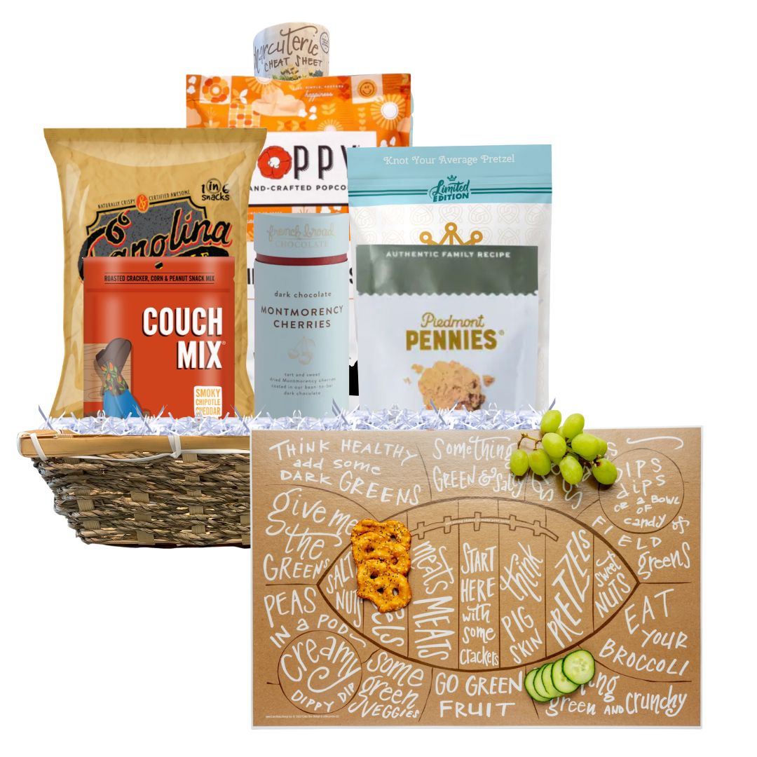 A Football Game Day Charcuterie Gift Basket featuring North Carolina-made snacks and a football-shaped charcuterie cheat sheet in front. Includes BBQ chips, spicy cheese biscuits, toffee popcorn, and more, presented in a reusable basket. Perfect for tailgates and parties.