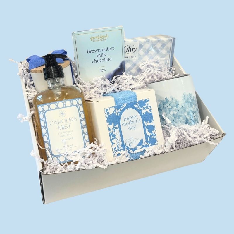 Angled view of the luxury Mother's Day gift box featuring spa-inspired gifts, NC-made chocolate, a floral tumbler, and elegant packaging in Carolina blue tones.