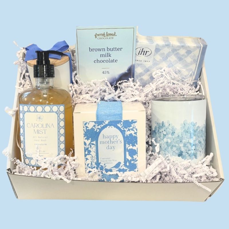 Elegant Mother’s Day gift box with spa-inspired hand soap, soy candle, floral tumbler, gingham napkins, and NC-made chocolate, beautifully packaged in Carolina blue tones.
