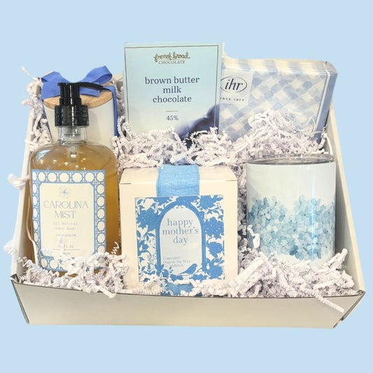 Elegant Mother’s Day gift box with spa-inspired hand soap, soy candle, floral tumbler, gingham napkins, and NC-made chocolate, beautifully packaged in Carolina blue tones.