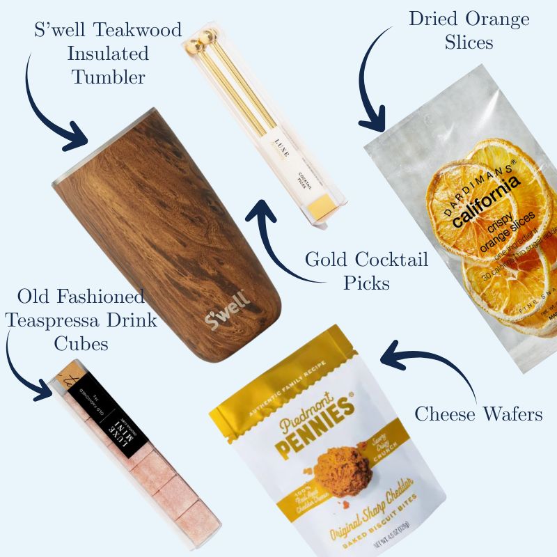 Flat lay of Men’s Old Fashioned Gift Box with labeled arrows pointing to each item: cocktail mixer cubes, dried orange slices, cheese wafers, teakwood tumbler, and gold cocktail picks, all displayed with descriptive text.