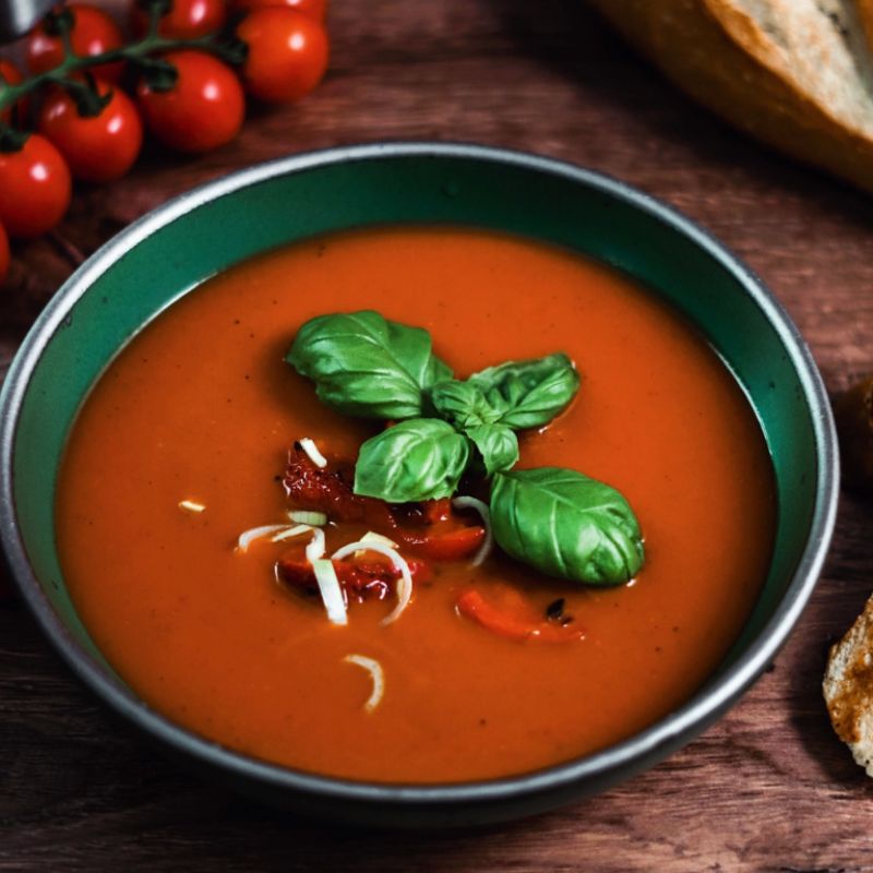 Tomato soup with basil leaves in a green bowl on a wooden table, made in NC