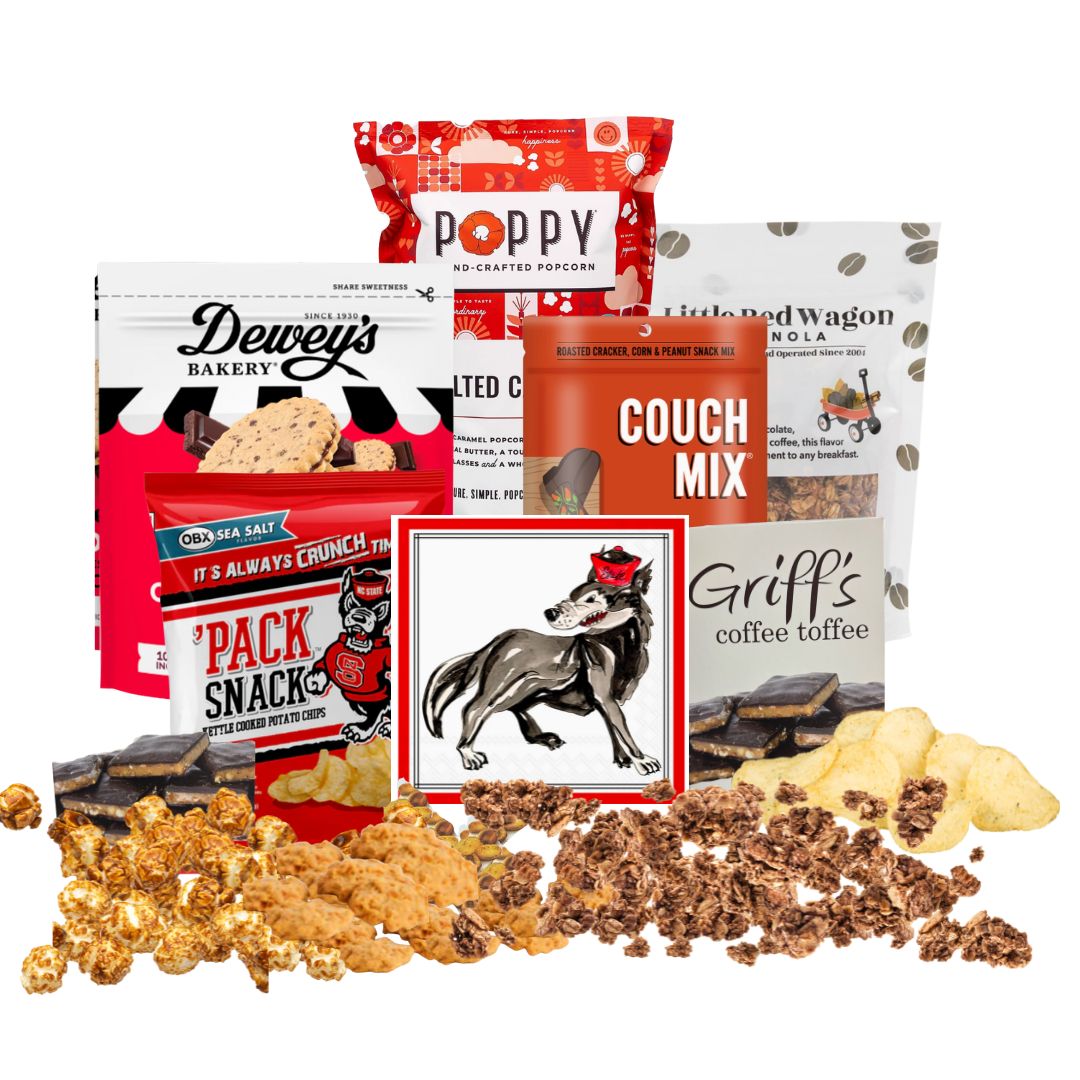 NC State-themed gift basket contents arranged on a countertop with small piles of each snack in front, showcasing red-packaged North Carolina-made gourmet treats