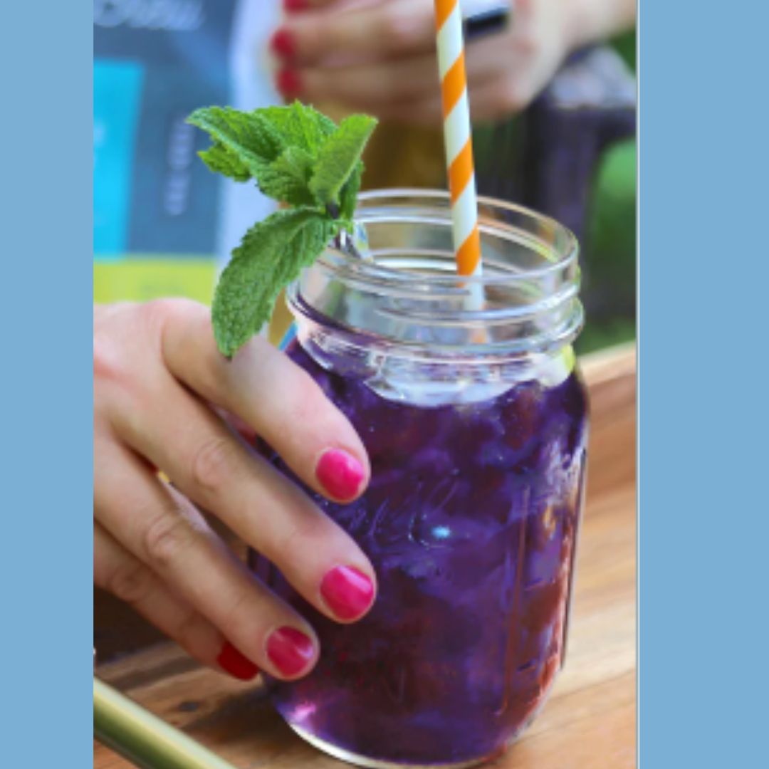 Blue Tea drink made by Asheville Tea Co. in a mason jar with a straw and mint leaf, held by a person with pink nail polish.