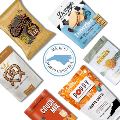 Flat lay image of the Carolina Crafted Gift Basket contents, featuring a variety of sweet and savory North Carolina-made snacks with a Made in NC emblem at the center.