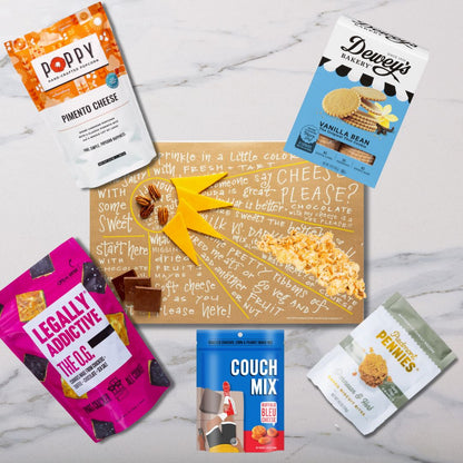 Top view of Sunburst Charcuterie Cheat Sheet surrounded by NC-made gourmet snacks like popcorn, cookies, and cheese wafers ready to create a delicious charcuterie board.