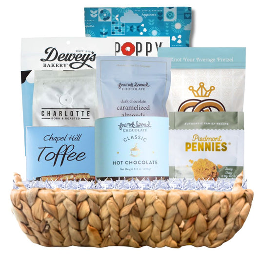 Luxury winter gift basket arranged in a woven hyacinth tray with gourmet North Carolina snacks, artisan coffee, chocolate, popcorn, and toffee in blue and white packaging suitable for Hannukah.