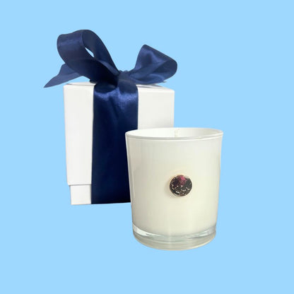 White candle with gold dogwood bloom emblem for the state of North Carolina with a decorative bow on a light blue background