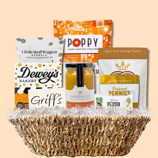 Beautifully arranged fall gourmet gift basket featuring made-in-North-Carolina snacks and treats, set against a soft light orange background that highlights the autumn theme