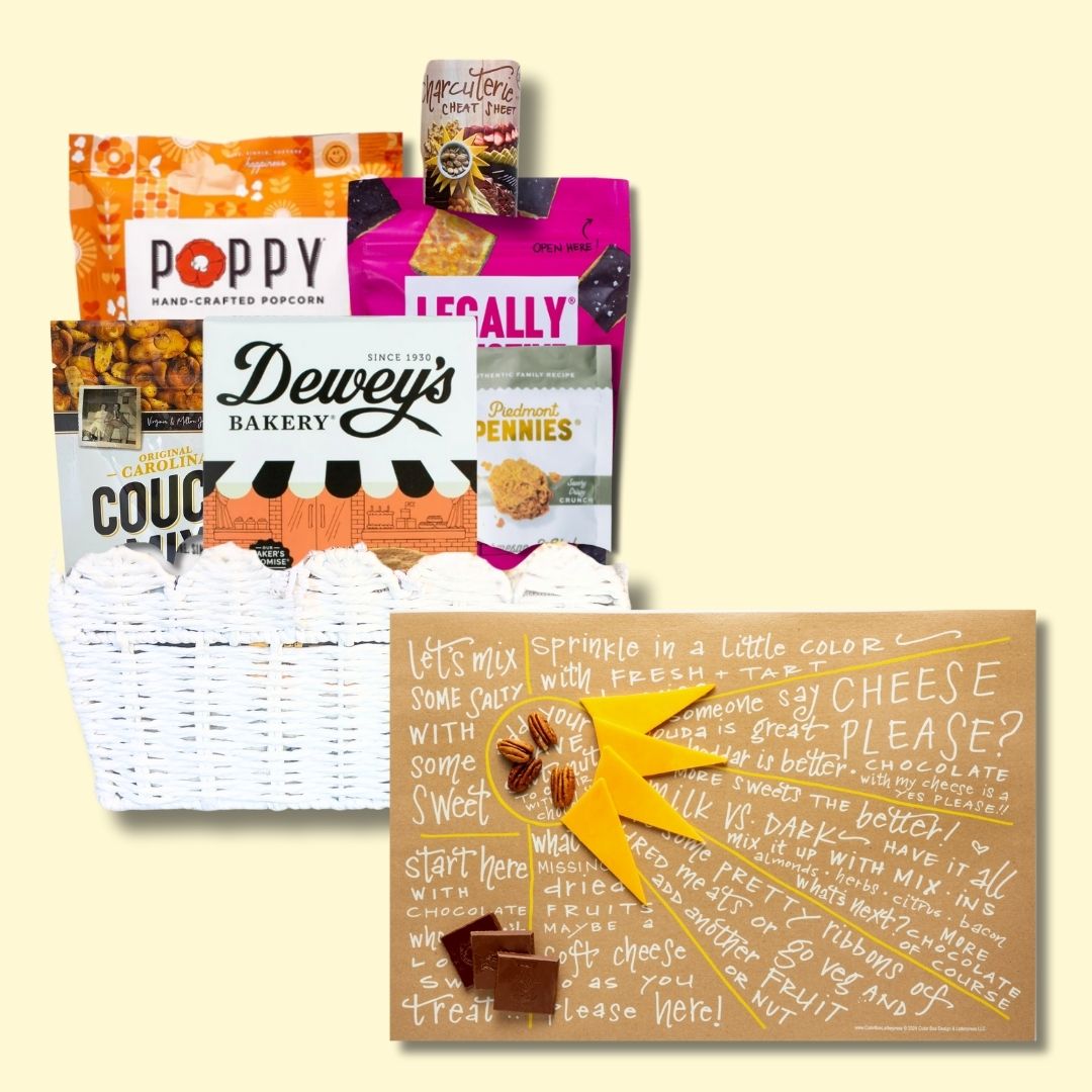 Sunburst Charcuterie Gift Basket with open cheat sheet against a light yellow background, highlighting NC-made gourmet treats like cookies, popcorn, and cheese wafers