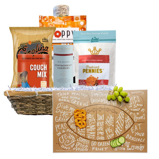 A Football Game Day Charcuterie Gift Basket featuring North Carolina-made snacks and a football-shaped charcuterie cheat sheet in front. Includes BBQ chips, spicy cheese biscuits, toffee popcorn, and more, presented in a reusable basket. Perfect for tailgates and parties.