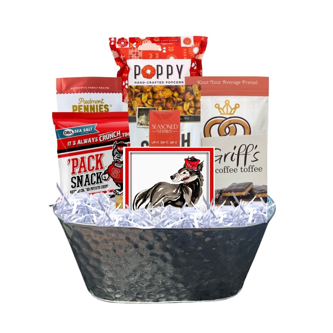 Assembled NC State-themed gourmet gift basket in a hammered tin planter, featuring red-packaged North Carolina-made snacks and watercolor wolf beverage napkins