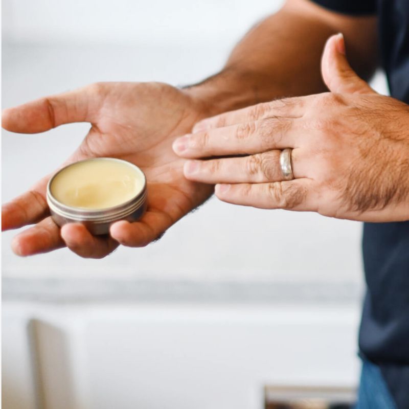 Person holding a small container of balm with another hand against a neutral background to show contents of southern comfort and care box