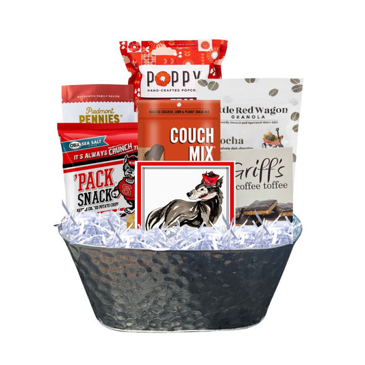 Assembled NC State-themed gourmet gift basket in a hammered tin planter, featuring red-packaged North Carolina-made snacks and watercolor wolf beverage napkins