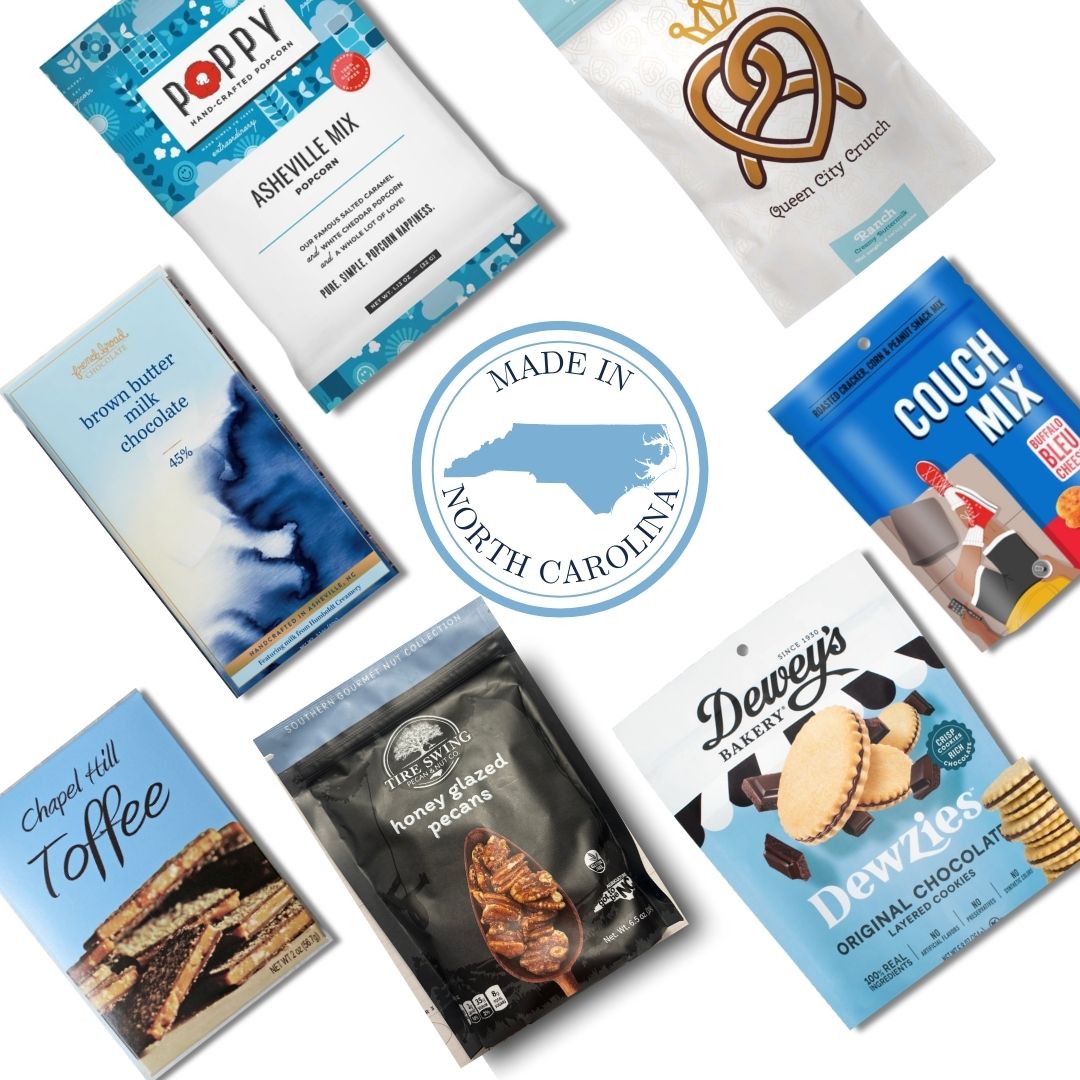 Flat lay of gourmet food products included in the Carolina Blue Deluxe Gift Basket, featuring NC-made snacks and a central "Made in North Carolina" icon.