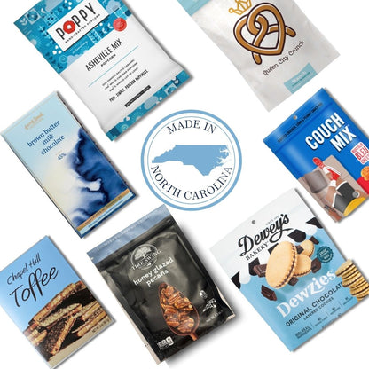 Flat lay of gourmet food products included in the Carolina Blue Deluxe Gift Basket, featuring NC-made snacks and a central "Made in North Carolina" icon.
