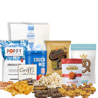 Carolina Snack Box with the white gift box displayed behind an arrangement of North Carolina-made gourmet snacks including popcorn, chips, cookies, granola, and toffee