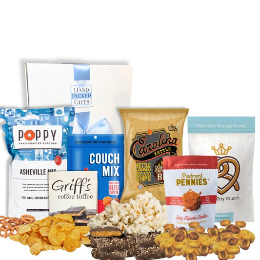 Carolina Snack Box with the white gift box displayed behind an arrangement of North Carolina-made gourmet snacks including popcorn, chips, cookies, granola, and toffee