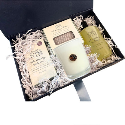 Open navy luxury gift box displaying lavender self-care items including a Dogwood soy candle, linen spray, body wash, and eye pillow for mothers day