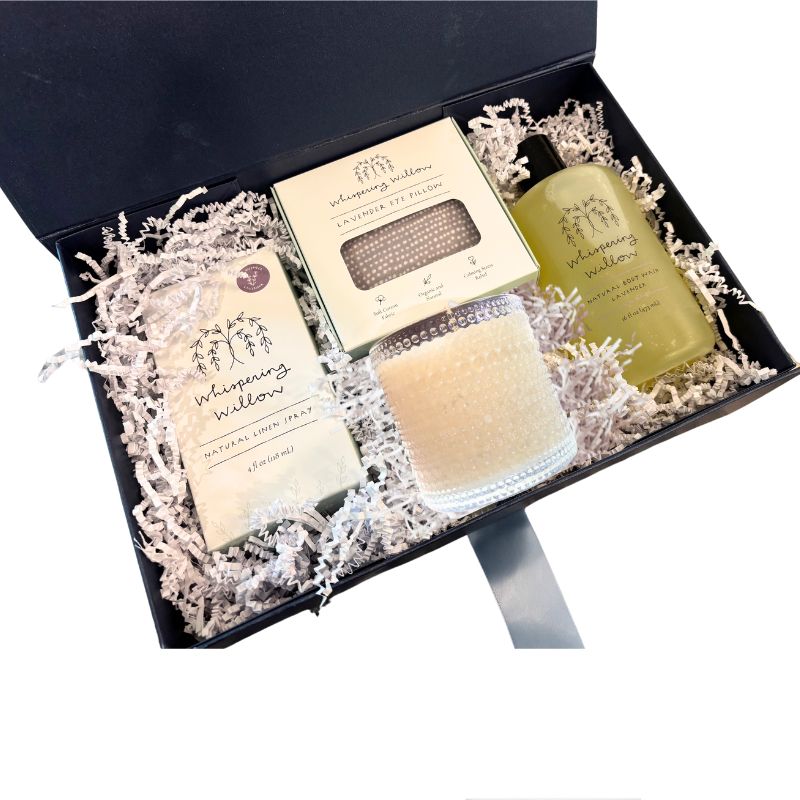 Open navy luxury gift box displaying lavender self-care items including a soy candle, linen spray, body wash, and eye pillow—perfect for relaxation and gifting