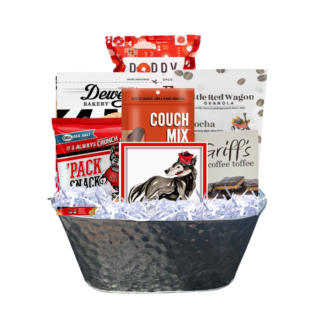 Assembled NC State-themed gourmet gift basket in a hammered tin planter, featuring red-packaged North Carolina-made snacks and watercolor wolf beverage napkins