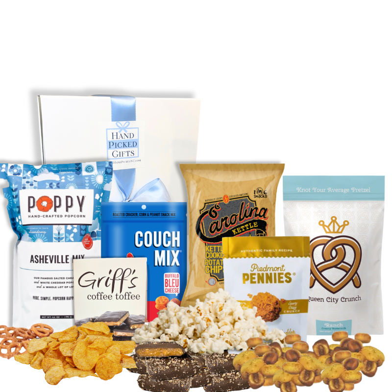 Carolina Snack Box with the white gift box displayed behind an arrangement of North Carolina-made gourmet snacks including popcorn, chips, cookies, granola, and toffee