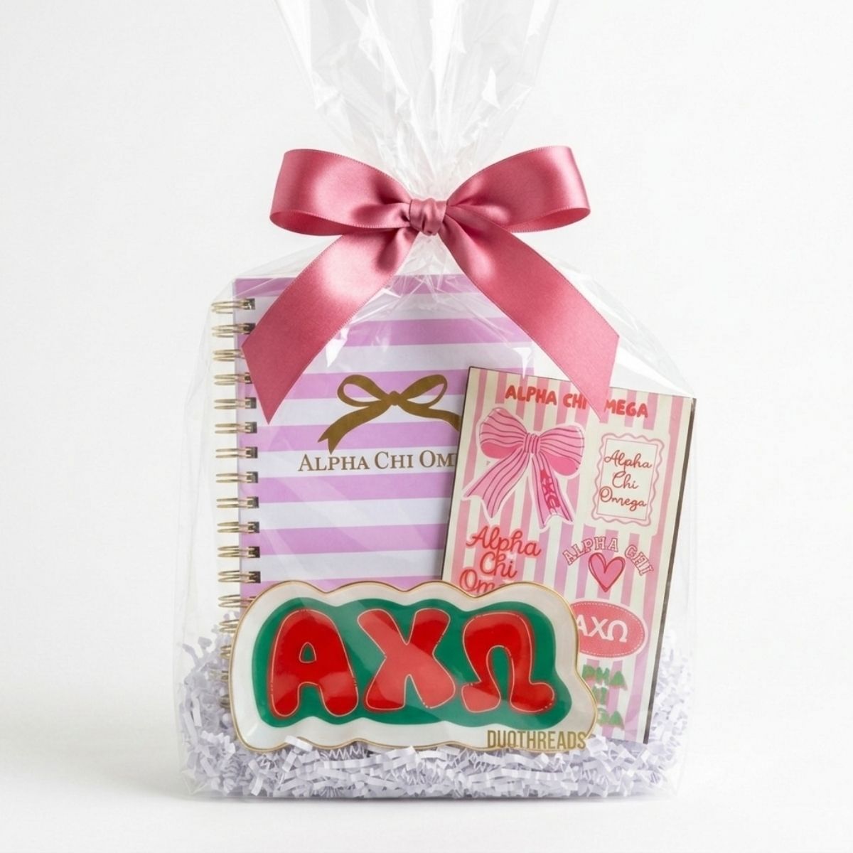 Gift set with Alpha Chi Omega theme, including a notebook, pen, and keychain, wrapped in cellophane with a pink bow.