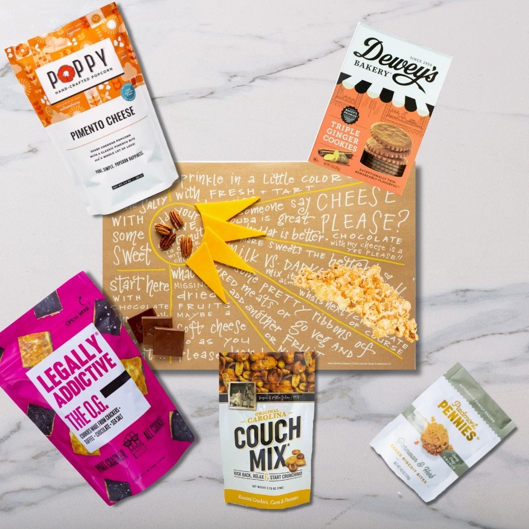 Top view of Sunburst Charcuterie Cheat Sheet surrounded by NC-made gourmet snacks like popcorn, cookies, and cheese wafers ready to create a delicious charcuterie board.