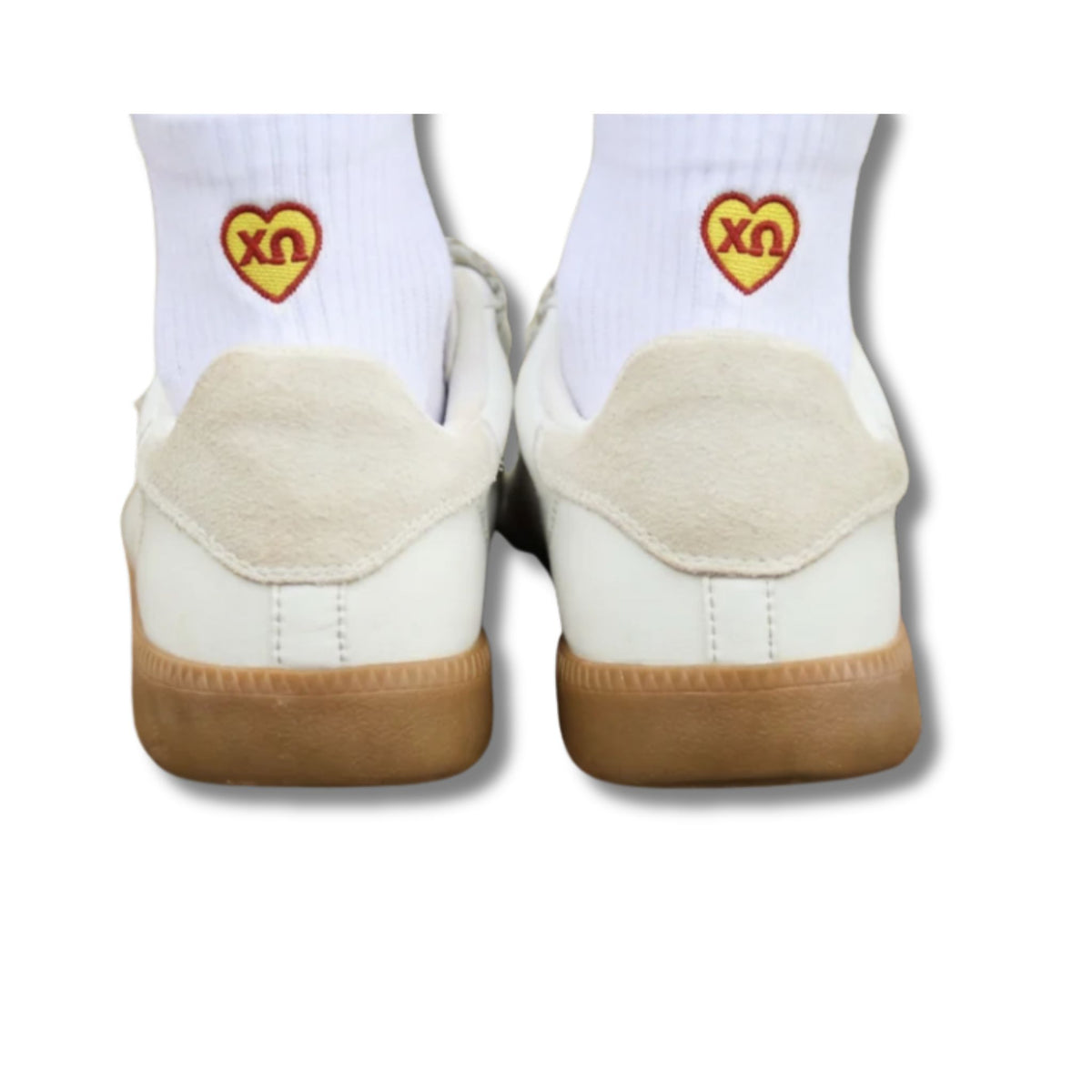 White low-top sneakers shown from the back, worn with white crew socks featuring a red heart patch with yellow Greek letters, Chi Omega, on a white background.