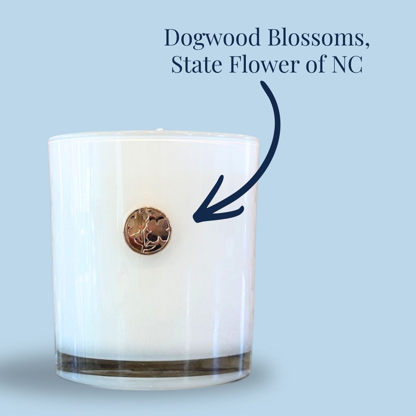 Close-up of gold dogwood blossom emblem on white glass candle, North Carolina state flower detail on luxury corporate gift