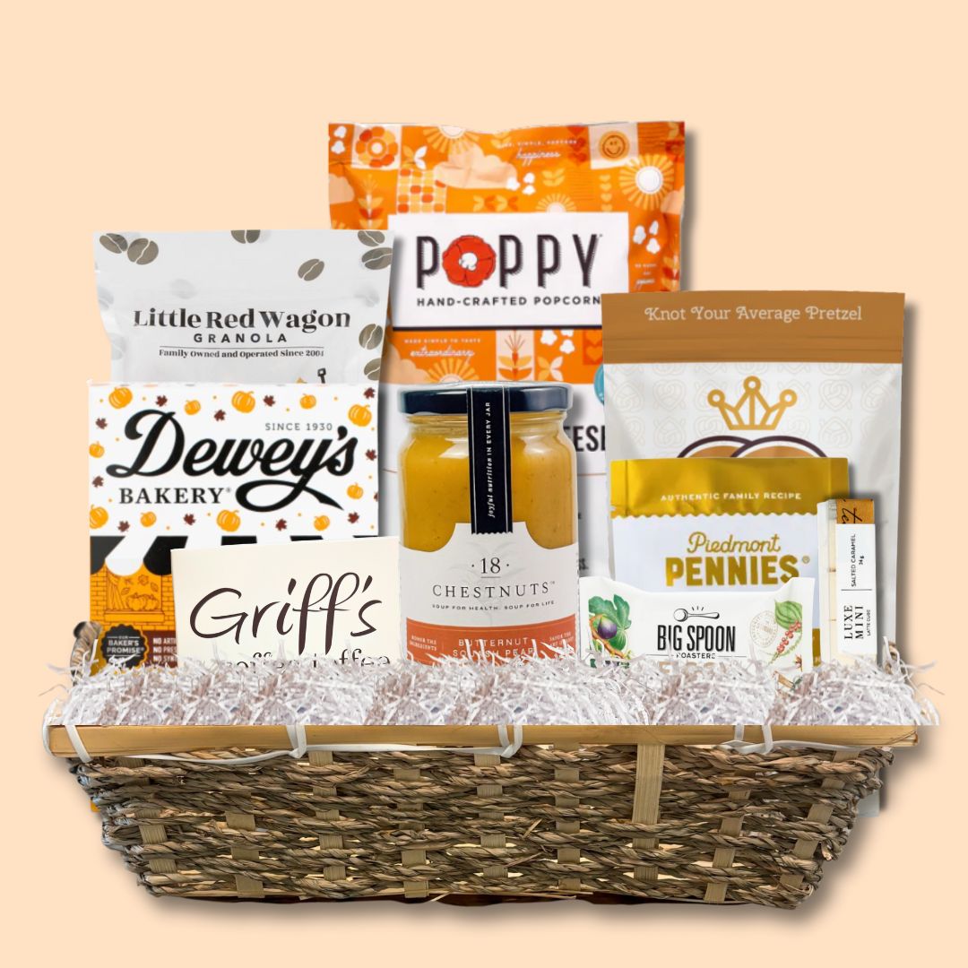 Beautifully arranged fall gourmet gift basket featuring made-in-North-Carolina snacks and treats, set against a soft light orange background that highlights the autumn theme