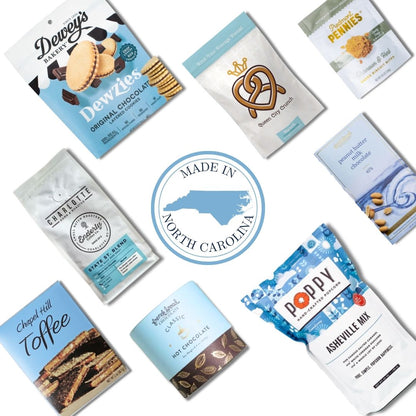 Flay lay of gourmet snacks and treats made in North Carolina, featuring popcorn, pretzels, cookies, toffee, hot chocolate mix, and chocolate from local NC makers, arranged around a central "Made in North Carolina" badge to highlight local, artisanal gift basket ingredients.