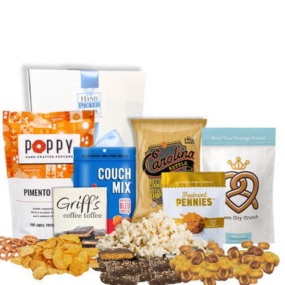 Carolina Snack Box with the white gift box displayed behind an arrangement of North Carolina-made gourmet snacks including popcorn, chips, cookies, granola, and toffee