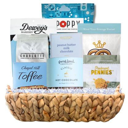 Luxury winter gift basket arranged in a woven hyacinth tray with gourmet North Carolina snacks, artisan coffee, chocolate, popcorn, and toffee in blue and white packaging suitable for Hannukah.